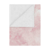Pink watercolor clouds minky baby blanket draped over a crib