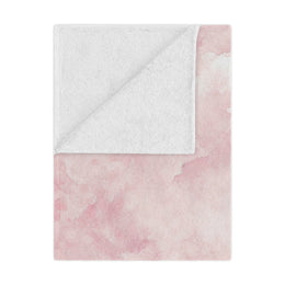 Pink watercolor clouds minky baby blanket draped over a crib