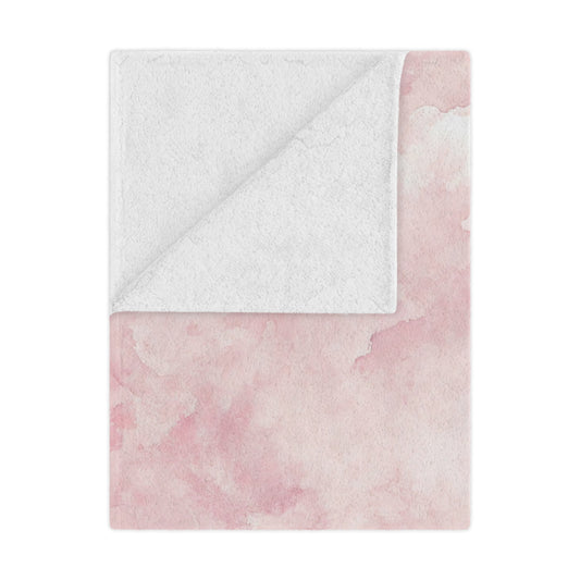 Pink watercolor clouds minky baby blanket draped over a crib